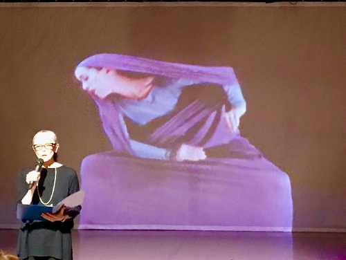 Janet Eilber, artistic director of the Graham Company, speaking to the audience about the 'Lamentation Variations,' with a film of Martha Graham's solo 'Lamentation' playing in the background.
